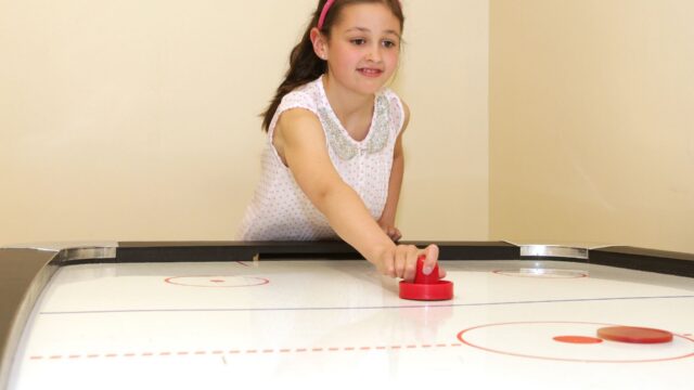Young girl enjoying air hockey in hotel's fun games room, creating joyful family moments for all ages.