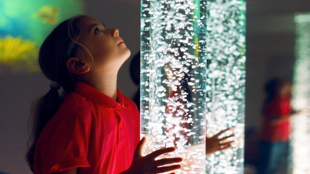 Child in therapy sensory stimulating room, snoezelen. Child interacting with colored lights bubble tube lamp during therapy session.