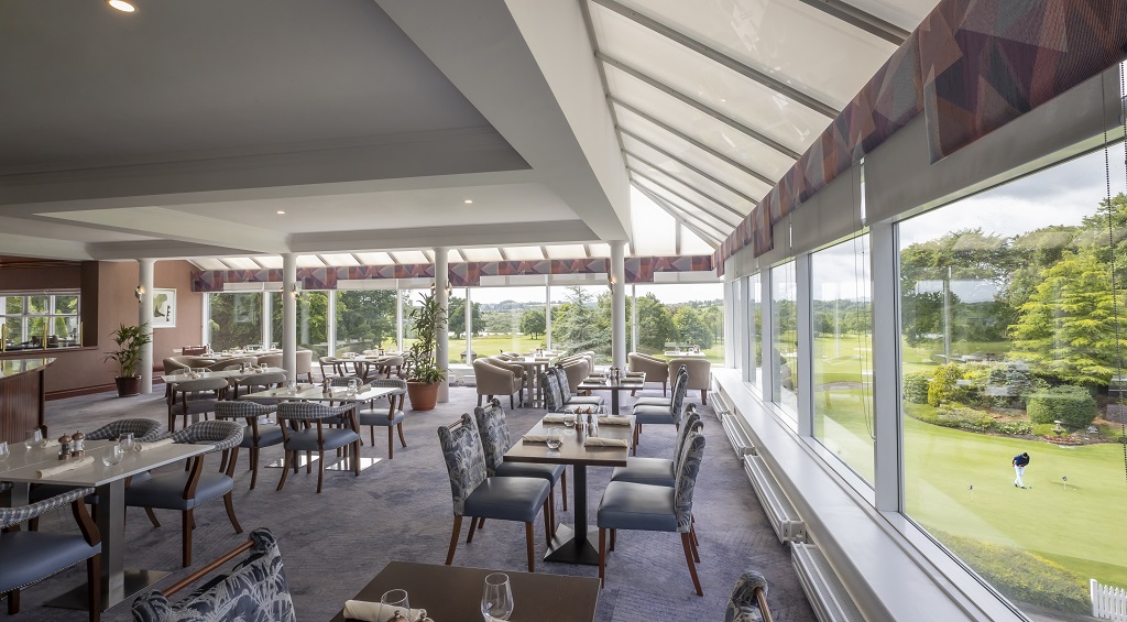 Bright dining area with large windows and golf course view, featuring elegant tables and chairs for a relaxing experience.