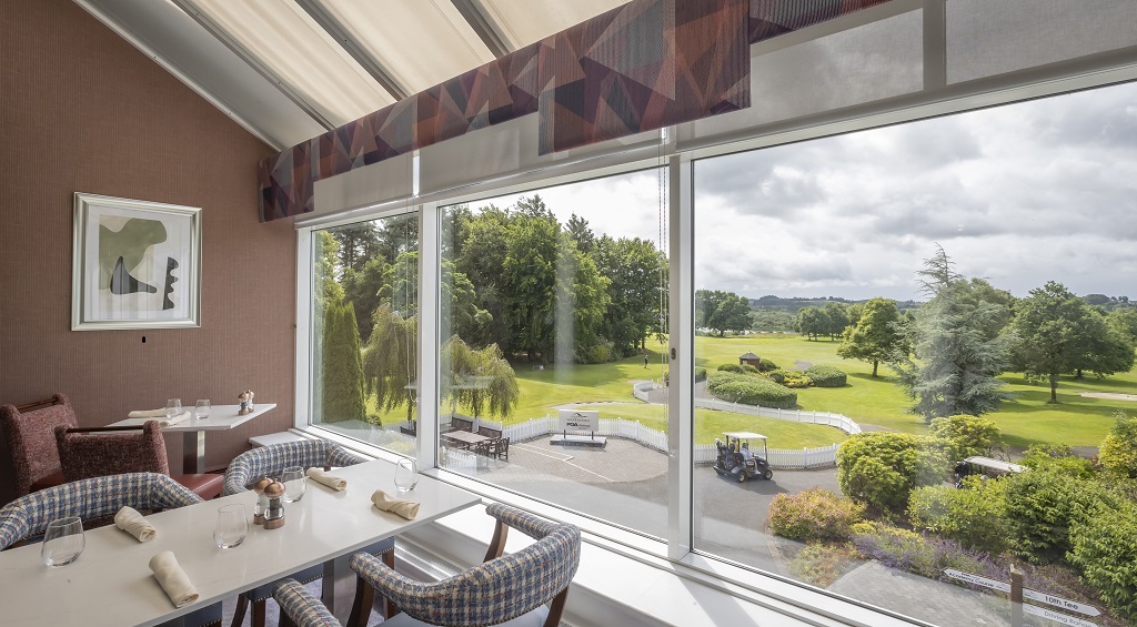 Cozy hotel dining area with panoramic golf course views, stylish seating, and lush greenery inviting a delightful experience.