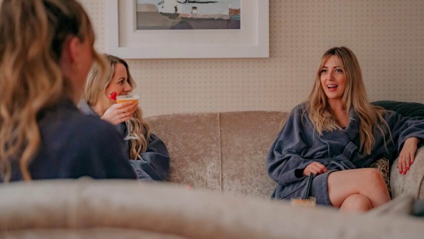 Guests relax in luxury hotel lounge, enjoying drinks in plush robes, surrounded by elegant decor and art.
