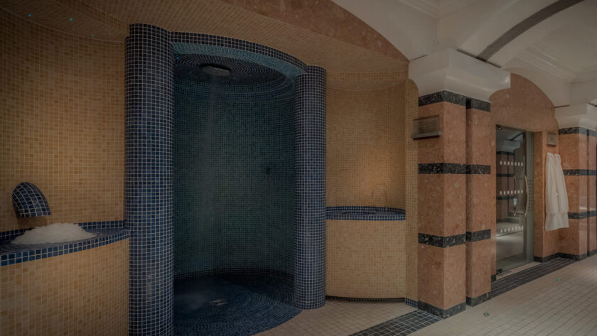 Relaxing hotel spa with elegant mosaic tiles, featuring steam showers and plush white robes for a luxurious retreat.